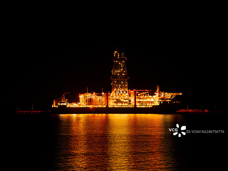 夜间，灯火辉煌的离岸石油钻井平台倒映在水中图片素材