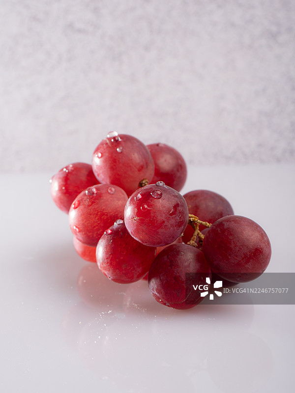 反光表面上带有水滴的新鲜红葡萄特写图片素材