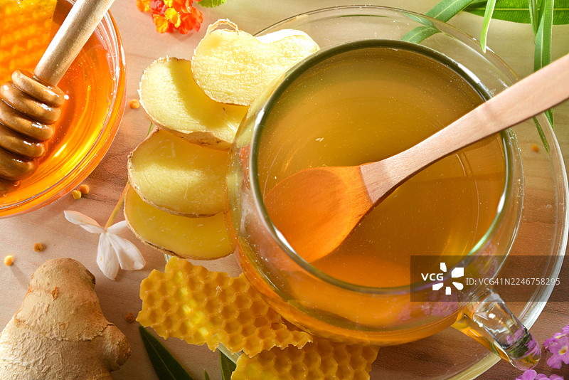 俯视角度拍摄的姜蜜茶，配有蜂蜜和蜂巢，摆放在木桌上，并点缀着新鲜姜片和鲜花。图片素材
