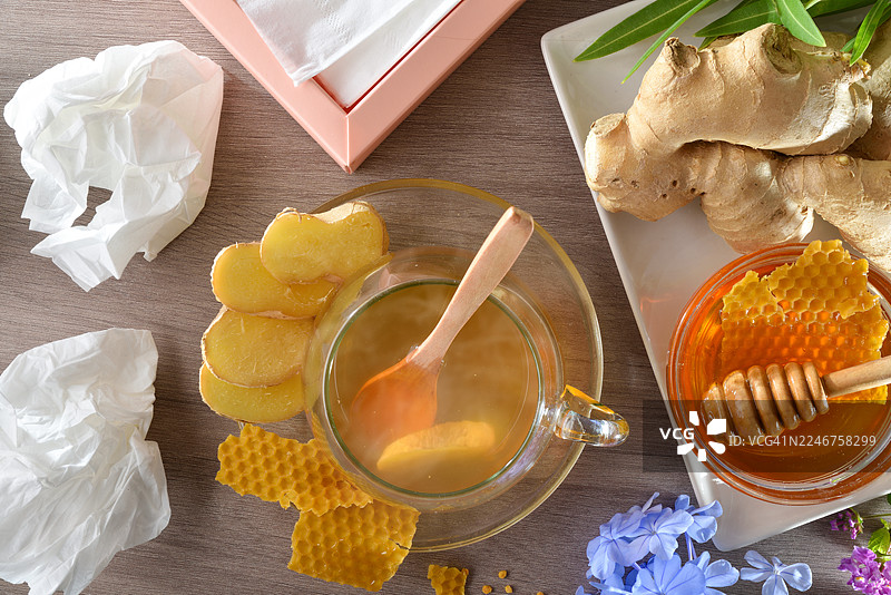 俯视角度拍摄的姜茶、蜂蜜和用过的纸巾放在木桌上，暗示着缓解感冒或流感的用品图片素材