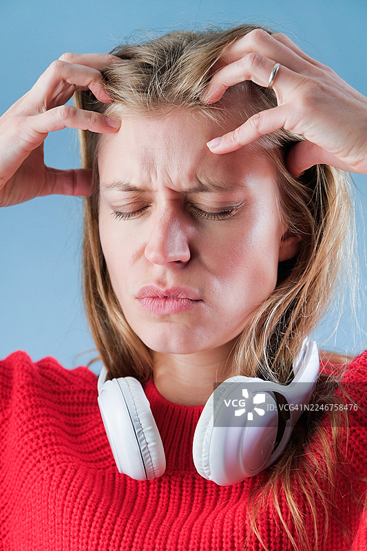 Frustrated woman with hands on head and headphones around neck, suffering from headache or stress图片素材