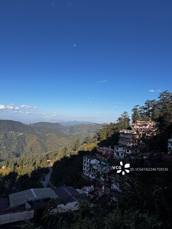 从高处俯瞰宁静的山城，背景是晴朗的蓝天和一轮明月，印度西姆拉市区图片素材