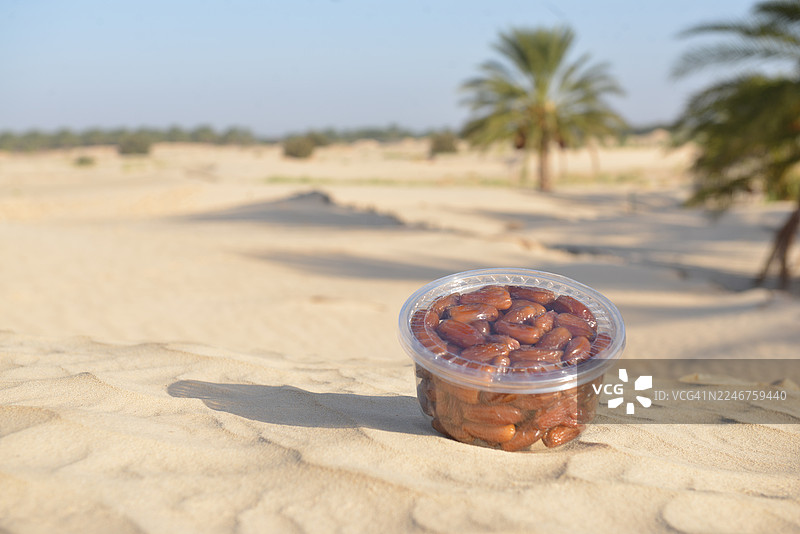 沙漠景观中，沙滩上的新鲜椰枣塑料容器，背景有棕榈树图片素材