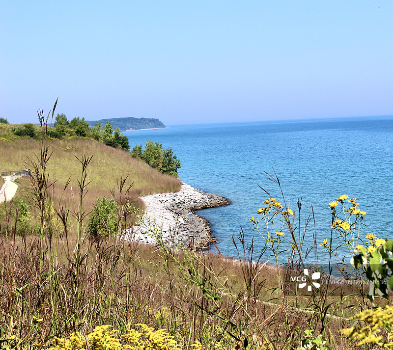 一望无际的宁静大海，衬托着湛蓝的天空，前景是崎岖的海岸线和郁郁葱葱的绿色山丘图片素材