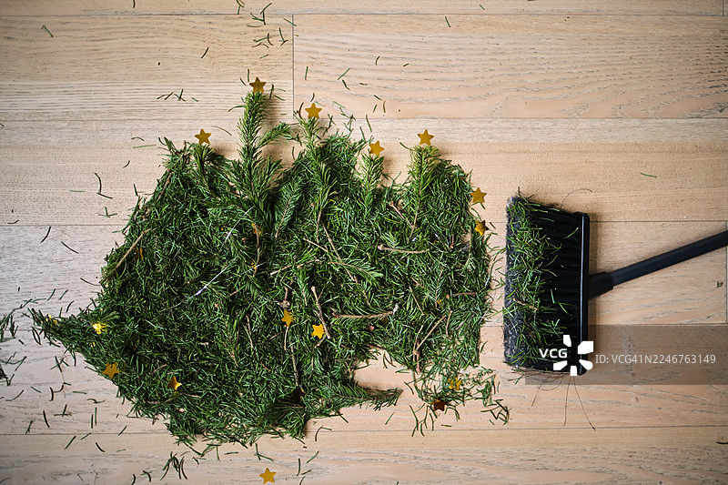圣诞节后，用扫帚清理木地板上的松针和金色小星星图片素材