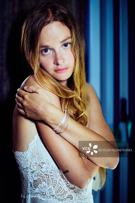 一位年轻美丽的女子长发，身穿蕾丝上衣，在昏暗的房间里直视镜头，表情微妙。图片素材