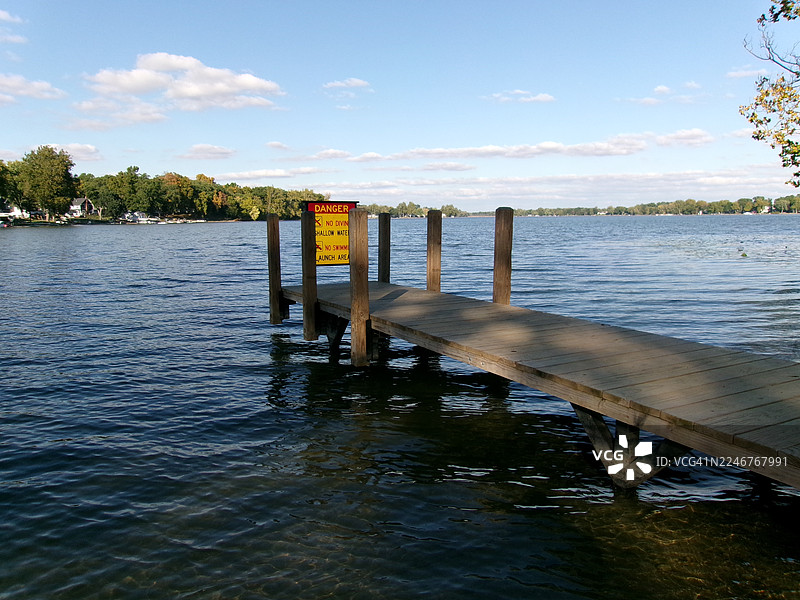 木制码头延伸入平静的湖泊，蓝天下的远方海岸线，美国波塔奇图片素材