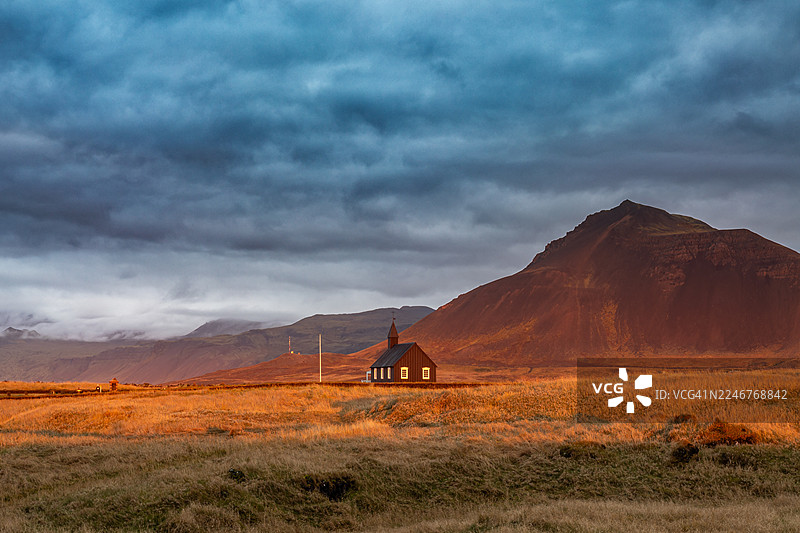 冰岛布迪尔黑教堂，夕阳下的金色田野与戏剧性的天空图片素材