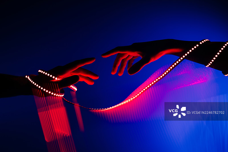 两只人手与发光的、波浪形的红光互动，在深蓝色背景下形成抽象而动态的连接。图片素材