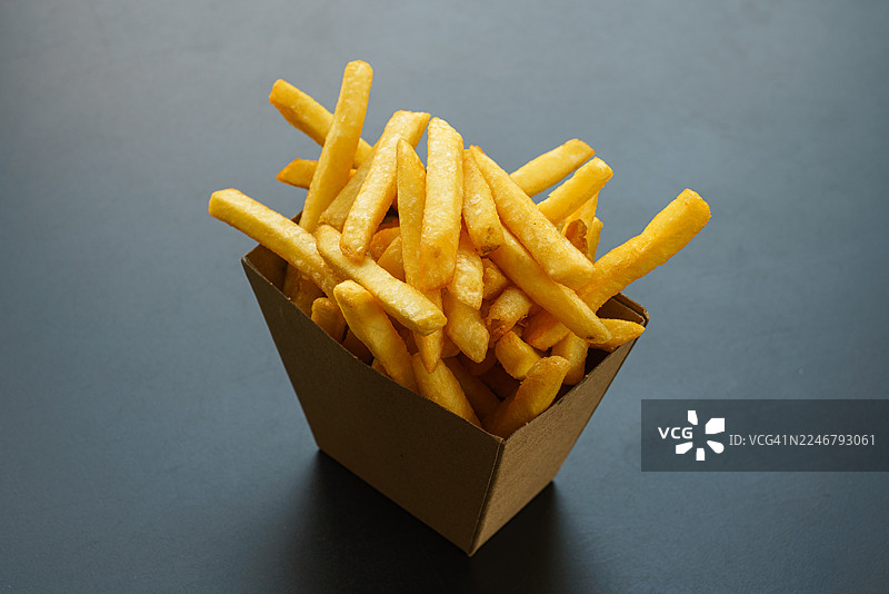 一次性餐盒里的炸薯条，背景为灰色。图片素材