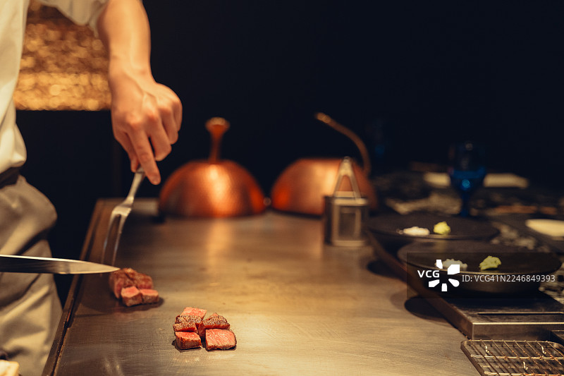 厨师在铁板烧烤架上为食客切熟牛排。图片素材