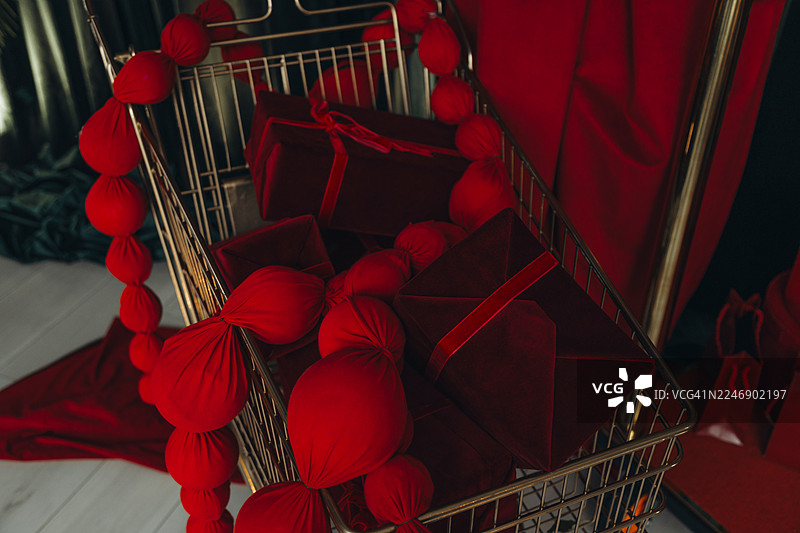 一个金色的购物篮里装着许多深红色的天鹅绒礼品盒和一个红色的布艺花环。图片素材