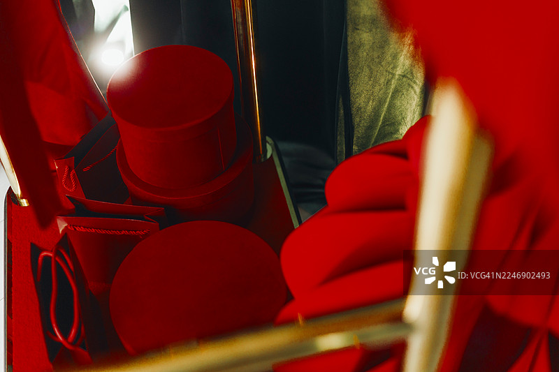 几个深红色圆柱形礼品盒和纸质礼品袋放在服务车上。图片素材