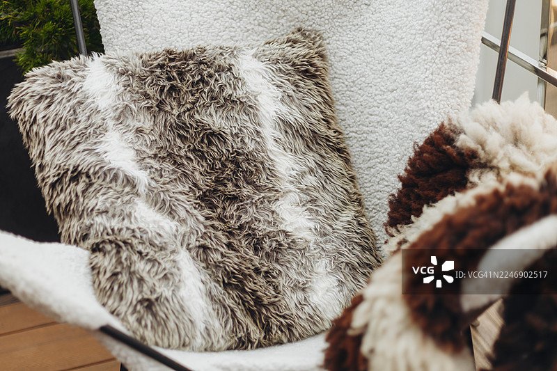 一个棕白相间的毛绒坐垫放在白色椅子上，背景是带有木地板和绿植的休息区。图片素材
