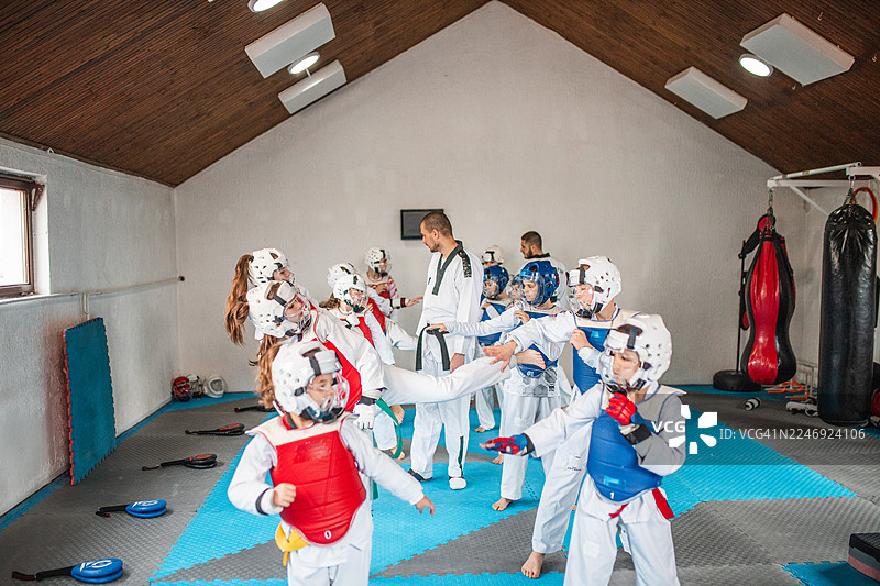 一群多元化的跆拳道学员正在练习动态腿踢和两人一组的对打训练图片素材