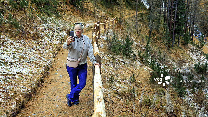秋季，一名女子在森林中的小路上倚靠着栅栏图片素材