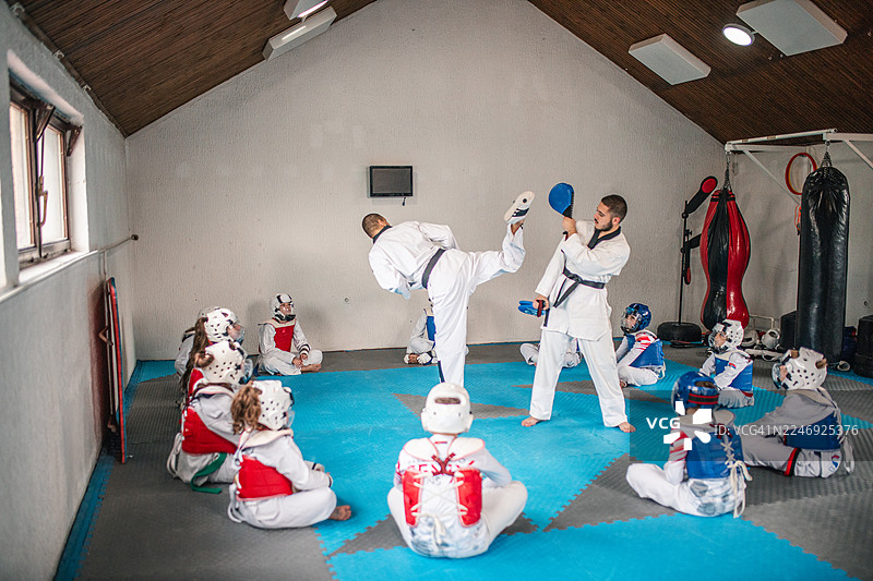 一群孩子正专注地看着两位跆拳道教练向他们展示踢腿动作图片素材