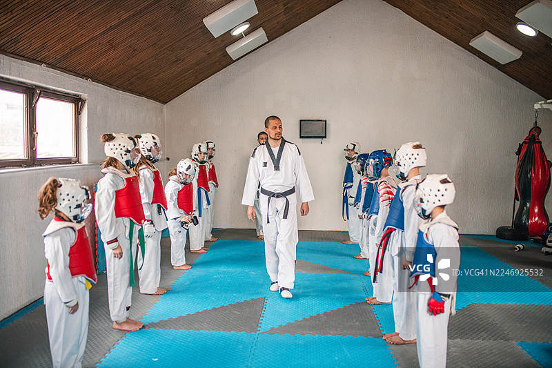 孩子们身穿带有红蓝腰带的白色跆拳道服，在两位武术教练的指导下练习跆拳道。图片素材
