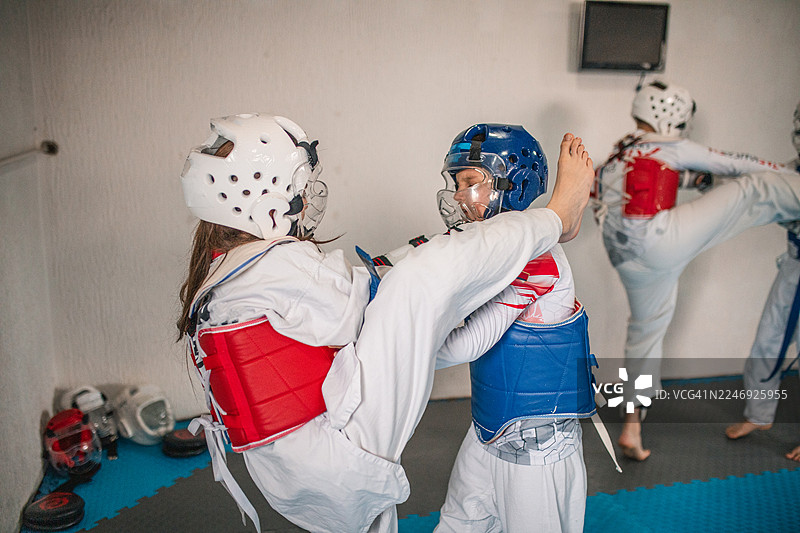 一群男孩和女孩穿着传统的白色跆拳道服和护具，在一个光线明亮的体育馆里激烈地进行搏击训练图片素材