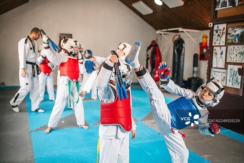 大量穿着传统白色跆拳道服和防护装备的运动员女孩和男孩正在激烈地进行对练图片素材