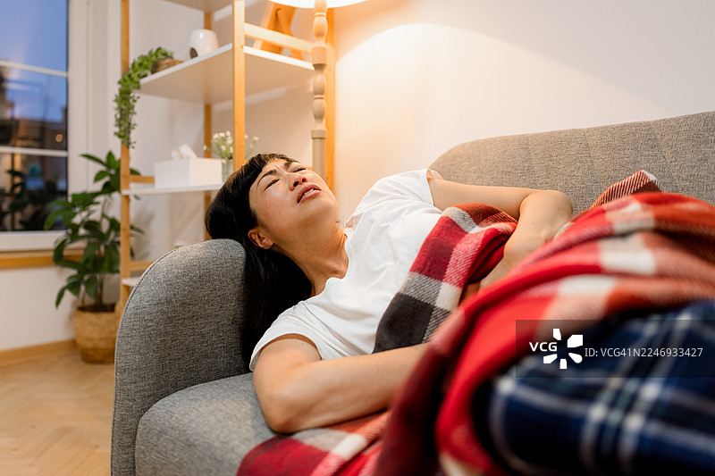 女子因胃部不适而微蜷在沙发上图片素材