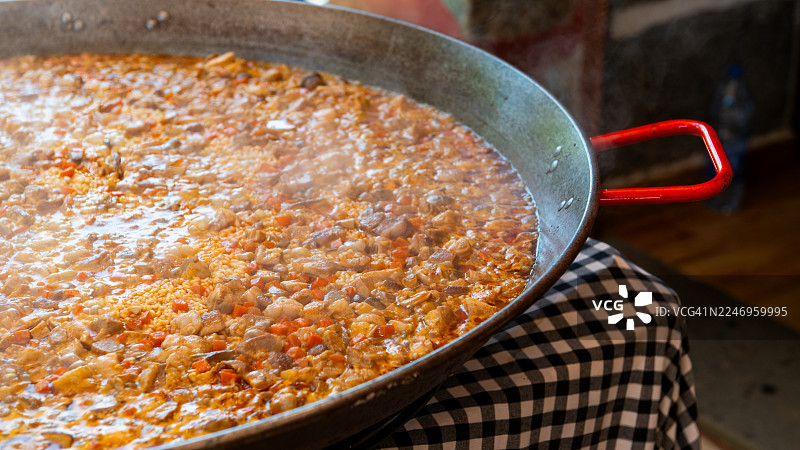 在一个大传统锅里烹饪冒着热气的西班牙海鲜饭，里面有米饭、肉类和蔬菜。图片素材