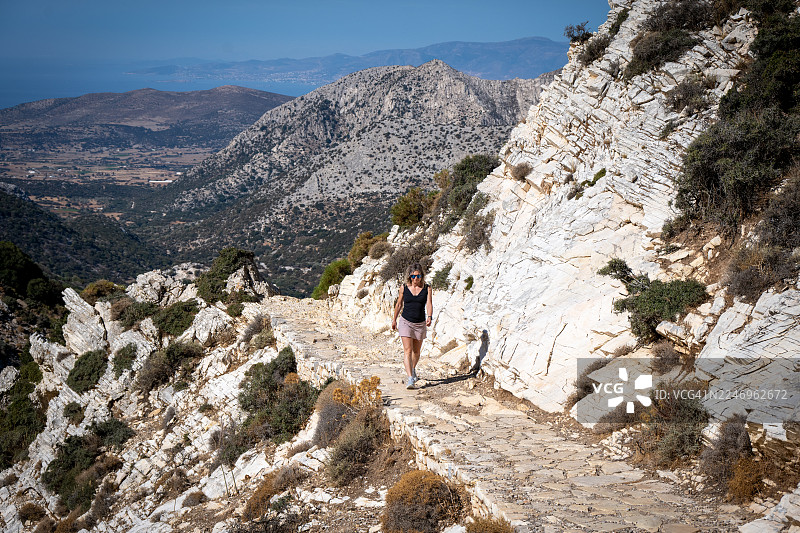 女子徒步登上扎斯山（宙斯山）。通往希腊基克拉泽斯群岛最高峰的岩石小径。希腊纳克索斯岛。图片素材