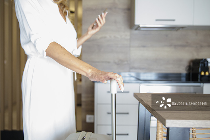 一位女士在室内拿着行李箱把手，正在查看手机图片素材
