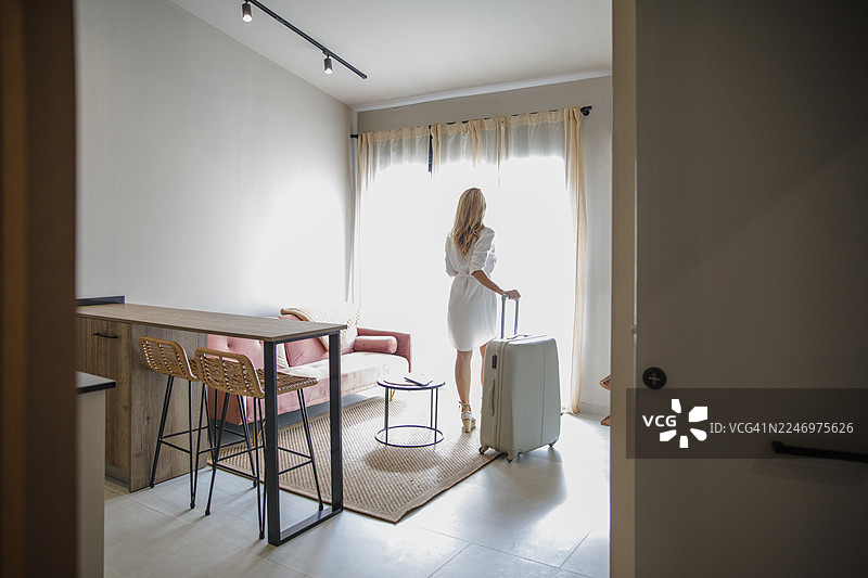 一位女士带着行李箱，站在明亮的公寓里，准备出行图片素材