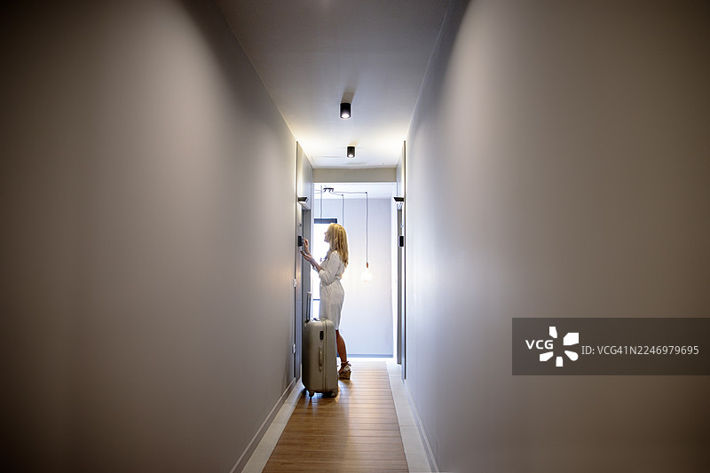 女人拖着行李箱，站在走廊的公寓门前图片素材