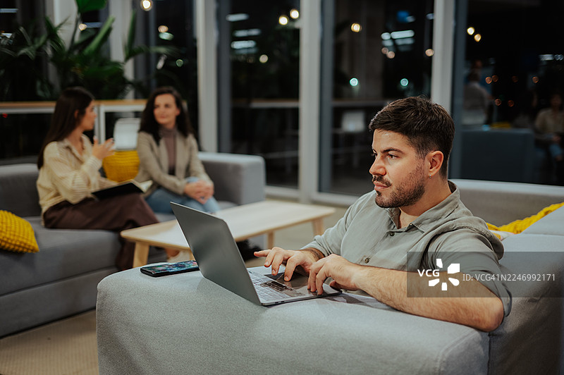 夜间在现代联合办公室内使用笔记本电脑工作的男人图片素材