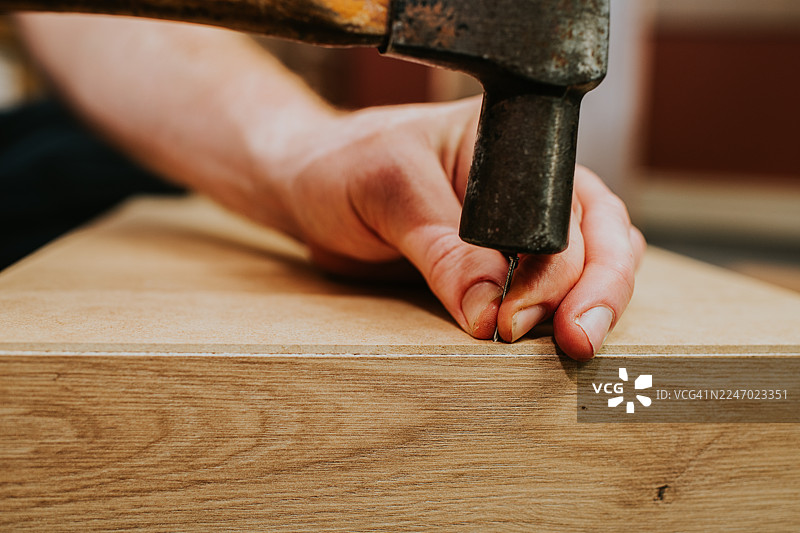 一名男子正在将图钉钉入他正在建造的木制橱柜图片素材