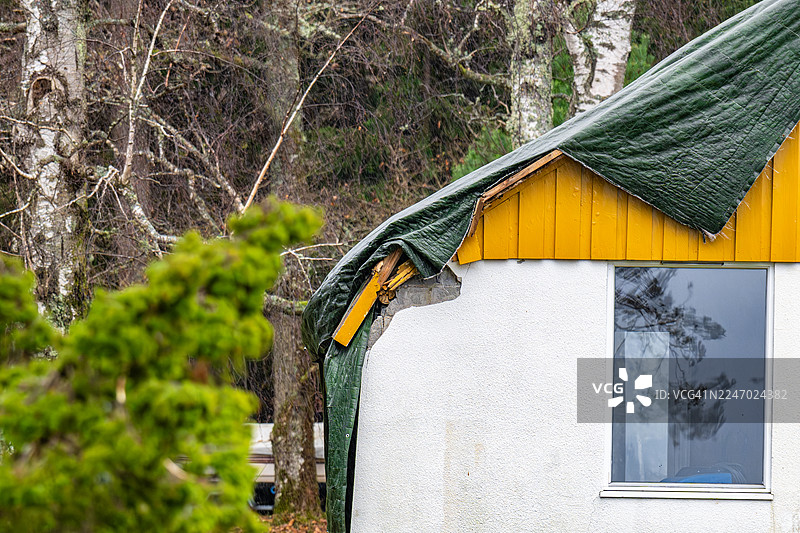 暴风雨导致一棵树倒在房屋上，摧毁了屋顶，现在屋顶上搭着防水布进行保护。图片素材