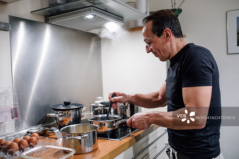 现代厨房里，男人在炉灶上用锅烹饪，蒸汽升腾图片素材
