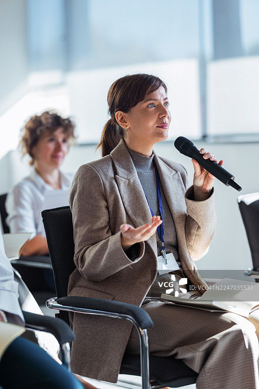 在现代办公室的商务会议中，一位职业女性正在对着麦克风讲话图片素材