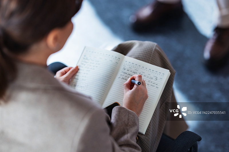 在休闲的办公室环境中，一个人正在进行笔记记录时在笔记本上书写图片素材