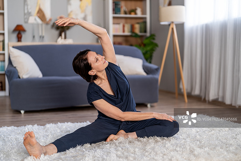 一位年长的女性在家中练习瑜伽拉伸以促进健康图片素材