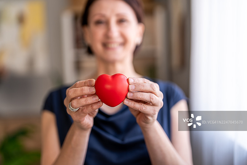 一位成熟的成年女性手持红色爱心，展现爱与关怀图片素材