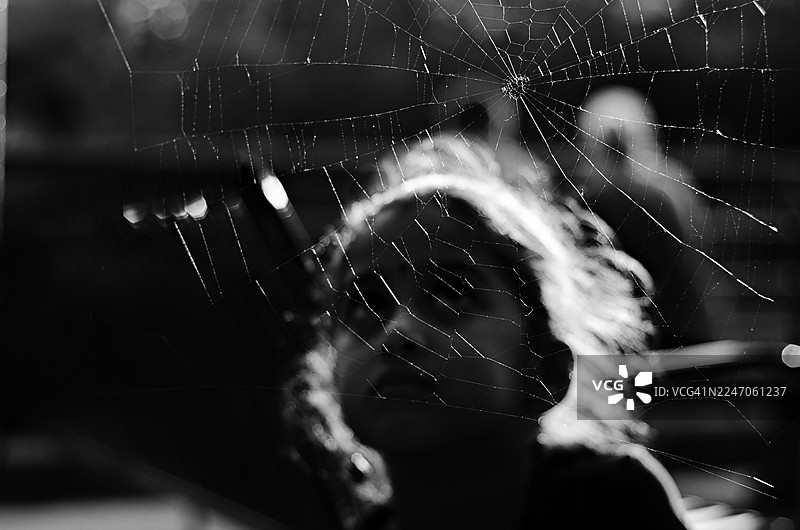 一名年轻女孩身穿黑白服装，透过一张细节精美的蜘蛛网凝视，蜘蛛网在前景中清晰对焦。这张黑白照片唤起了奇妙感、不同的视角以及大自然精致之美。图片素材