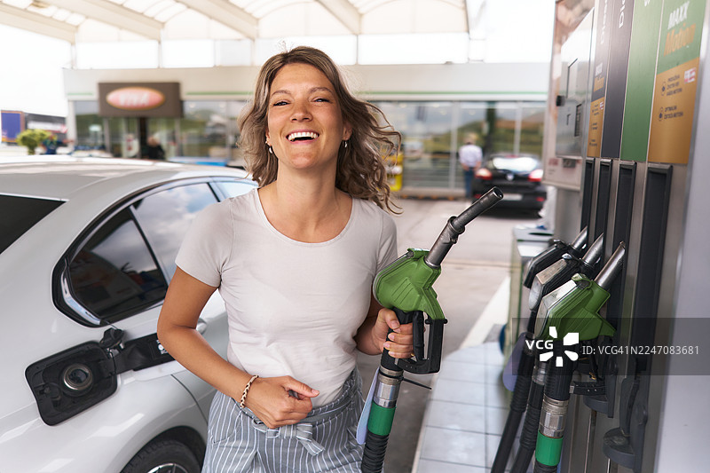 快乐的女士在加油站给汽车加油。图片素材