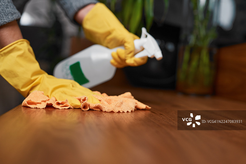 清洁中：戴手套的手用喷壶和抹布擦拭木桌图片素材