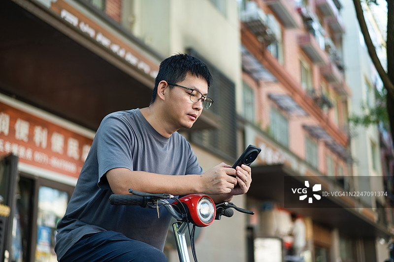 骑自行车的人在城市店面前使用手机图片素材