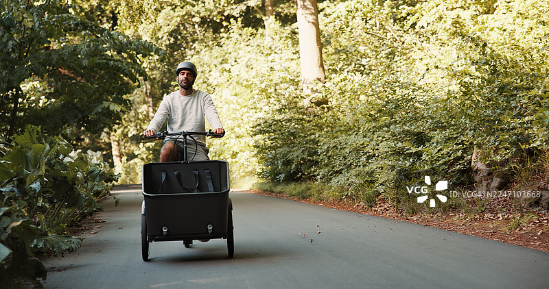 男人在自然风光中骑自行车，车上载有拖车，适合公路旅行、度假或街头出行。这位男士是旅行者或骑行者，戴着头盔，使用拖车作为环保交通工具、通勤或骑行。图片素材
