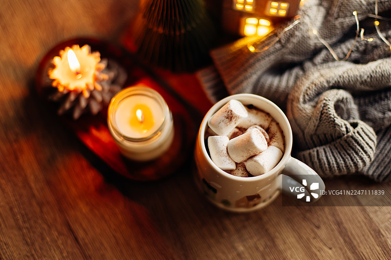 舒适的冬日景象，热巧克力上点缀着棉花糖，周围是节日装饰、烛光和柔软的织物，营造出温馨的氛围。图片素材