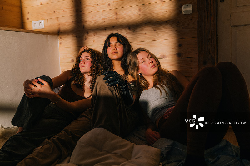 三个朋友在阳光明媚、温暖舒适的木墙房间里放松图片素材