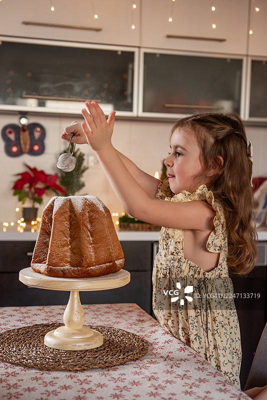 小女孩在圣诞节往潘多洛蛋糕上撒糖粉图片素材