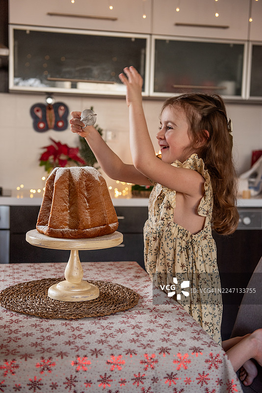 小女孩在圣诞节为潘多罗蛋糕撒上糖粉图片素材