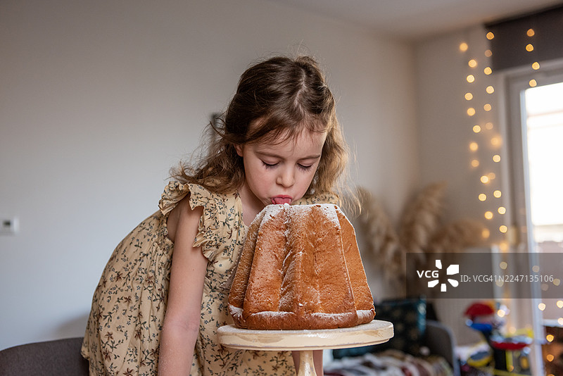小女孩正舔着潘多洛蛋糕上的糖粉图片素材