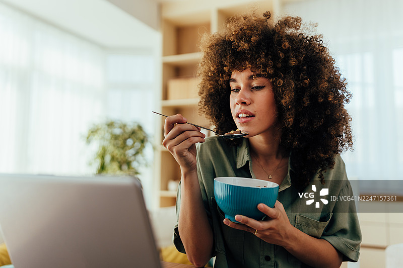 一位女性在用笔记本电脑工作时吃早餐麦片图片素材