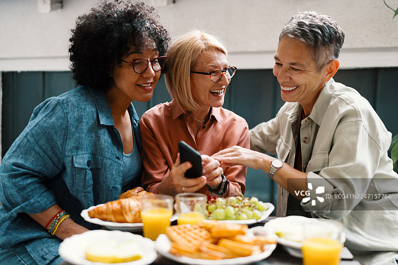 阳光明媚的露台上，快乐的女性在浏览在线约会和社交图片素材